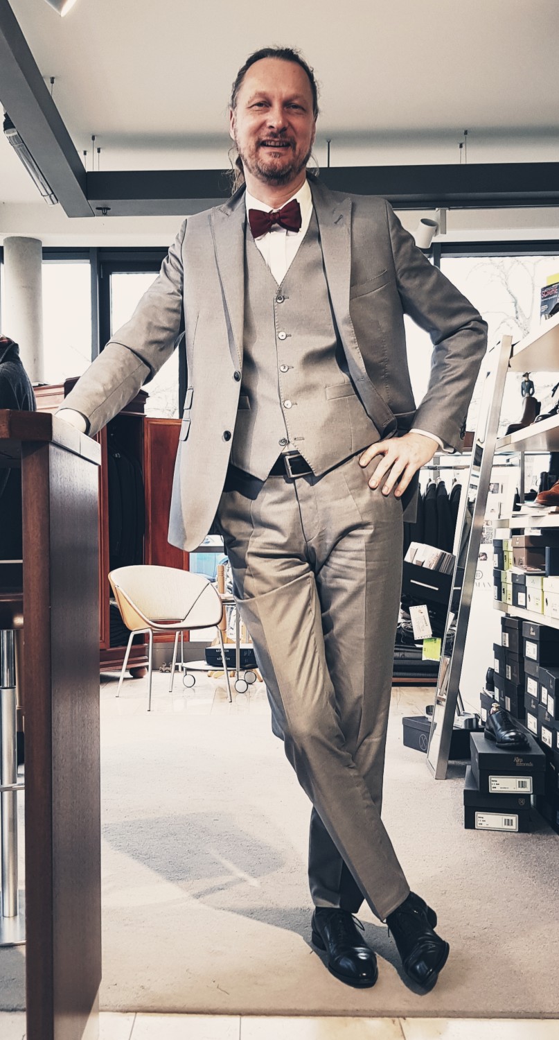 Rebmann Fashion: Leitbild - Ulrich Dörflinger im dreiteiligen hellgrauen Anzug mit roter Schleife